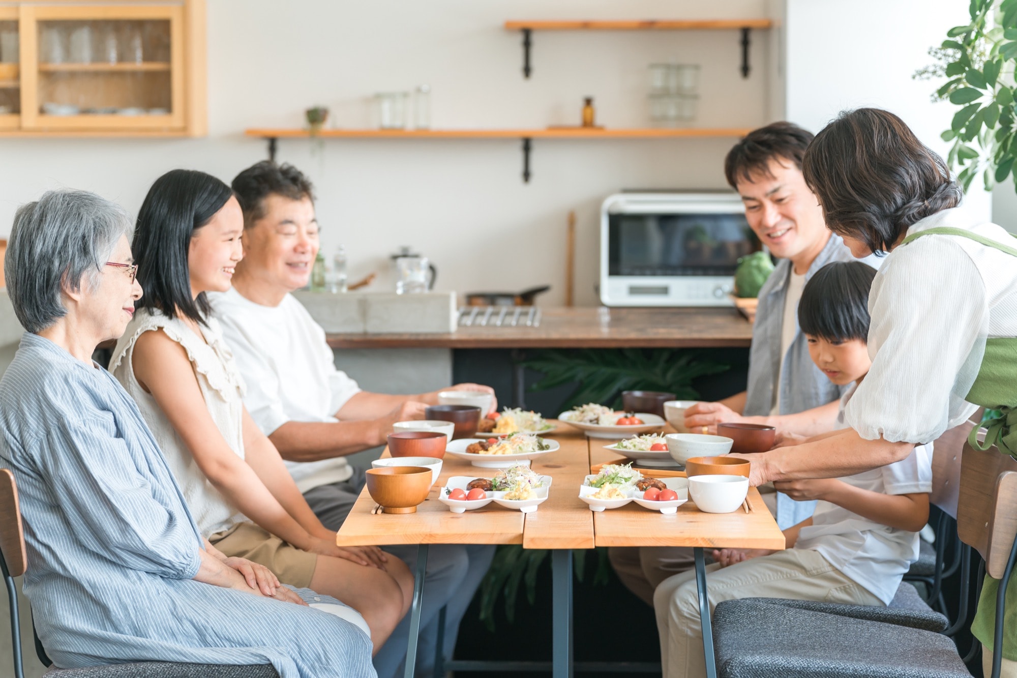 家のダイニングで家族団欒して食事する子供と夫婦・親子・三世代家族