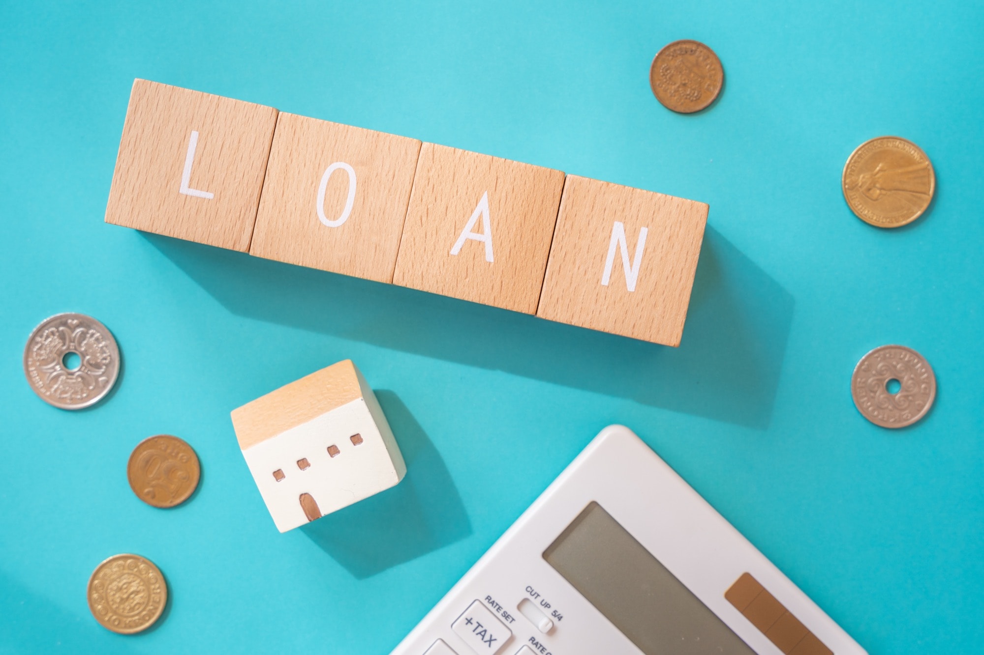 「LOAN」と書かれた積み木ブロックとおもちゃの家と電卓と小銭